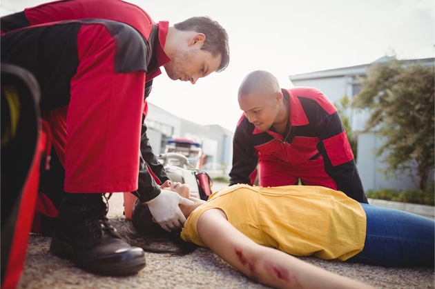 Emergency professionals dressed in red coveralls attending an injured patient laying on the ground