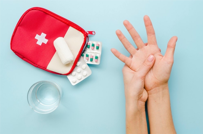First aid supplies on a blue surface, and a person's hand stretched out with the other hand pressing it