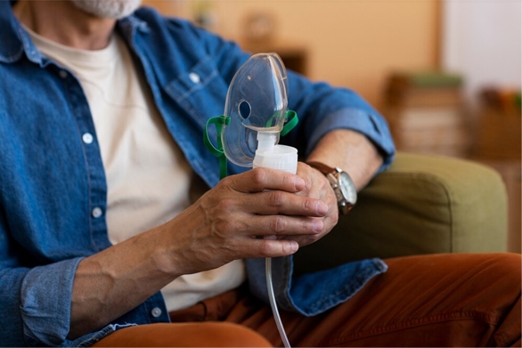Man in blue shirt holding asthma treatment equipment (nebulator mask)